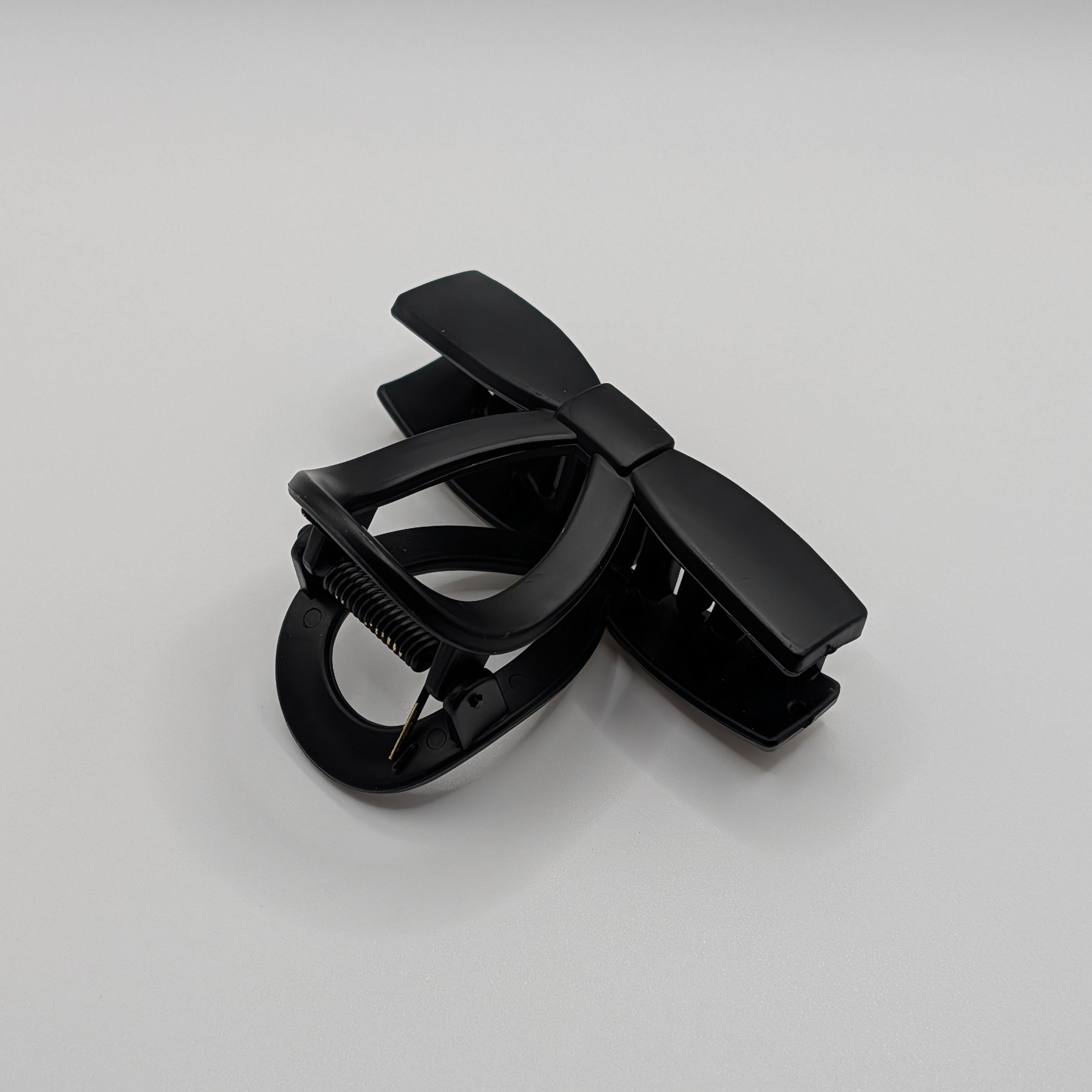 Angled view of a matte black minimalist bow-shaped hair claw clip.	

Schrägansicht einer mattschwarzen, minimalistischen Haarklammer in Schleifenform.
