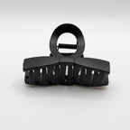 Front perspective of a black matte bow-tie hair claw clip with strong teeth.

Frontalansicht einer schwarzen matten Schleifen-Haarklammer mit starken Zähnen.