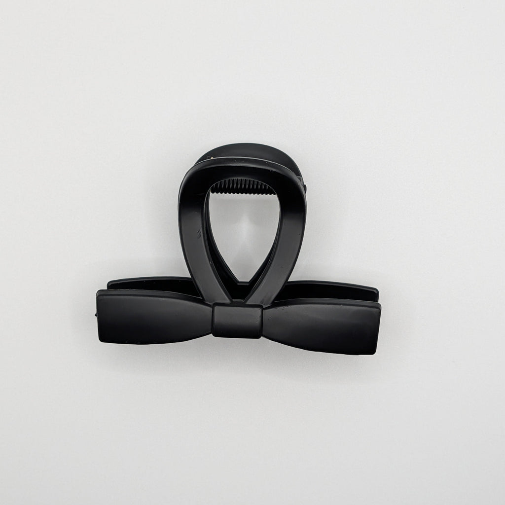 Top-down view of a matte black hair clip showing the sleek bow silhouette.

Draufsicht auf eine mattschwarze Haarklammer, die die elegante Schleifen-Silhouette zeigt.