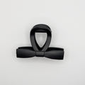 Top-down view of a matte black hair clip showing the sleek bow silhouette.

Draufsicht auf eine mattschwarze Haarklammer, die die elegante Schleifen-Silhouette zeigt.