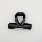 Top-down view of a matte black hair clip showing the sleek bow silhouette.

Draufsicht auf eine mattschwarze Haarklammer, die die elegante Schleifen-Silhouette zeigt.
