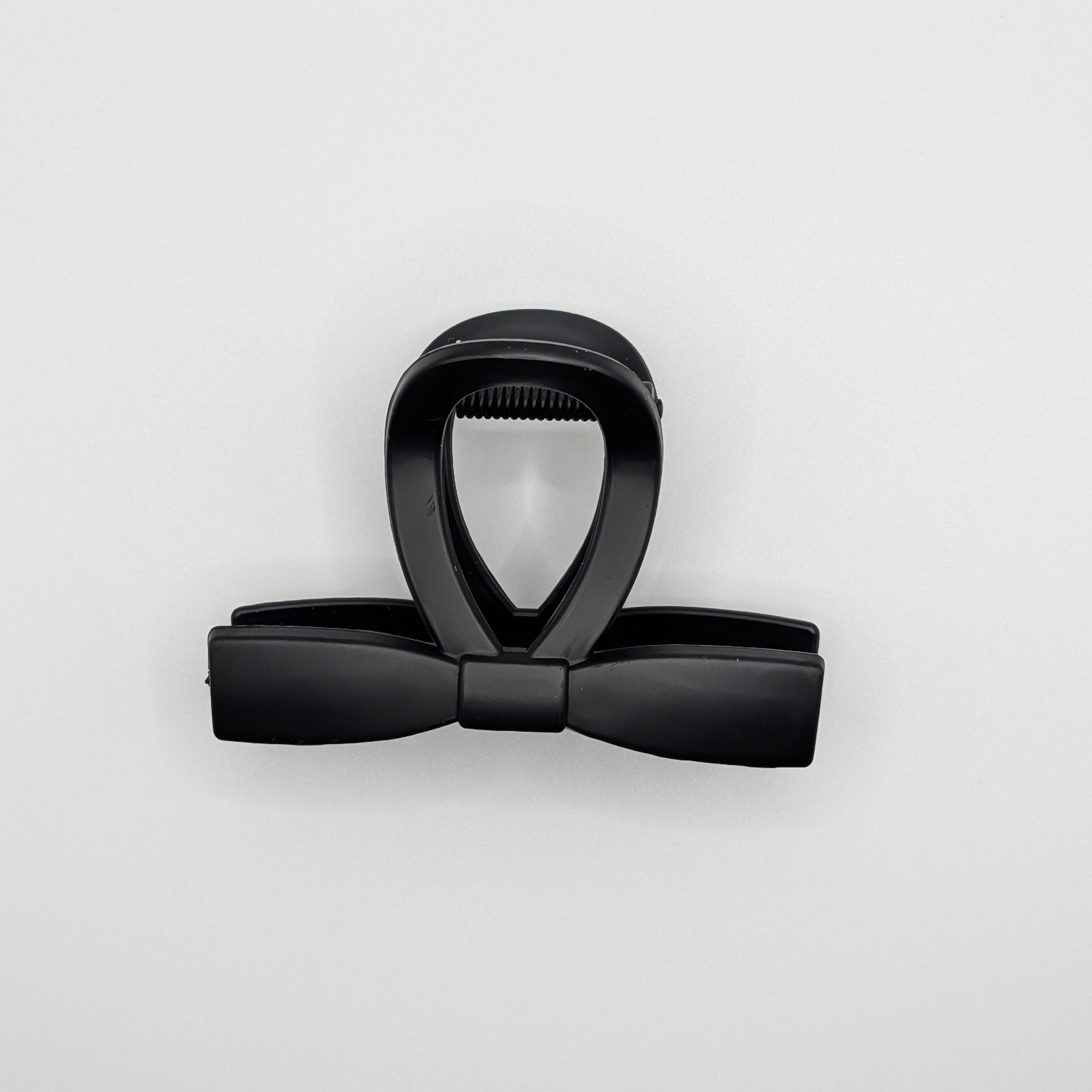Top-down view of a matte black hair clip showing the sleek bow silhouette.

Draufsicht auf eine mattschwarze Haarklammer, die die elegante Schleifen-Silhouette zeigt.