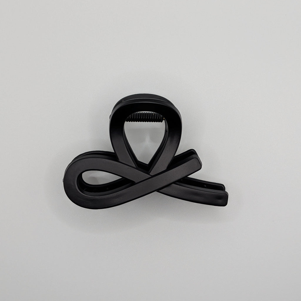 Matt Schwarz - Side view of a minimalist black infinity loop hair clip on a white background.	

Seitenansicht einer minimalistischen schwarzen Unendlichkeits-Haarklammer auf weißem Hintergrund.