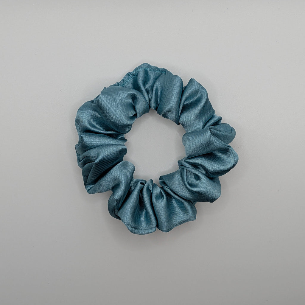 klein - Flatlay of a shimmering blue silk-style satin scrunchie.	

Flatlay eines schimmernden blauen Satin-Haargummis im Seiden-Stil.