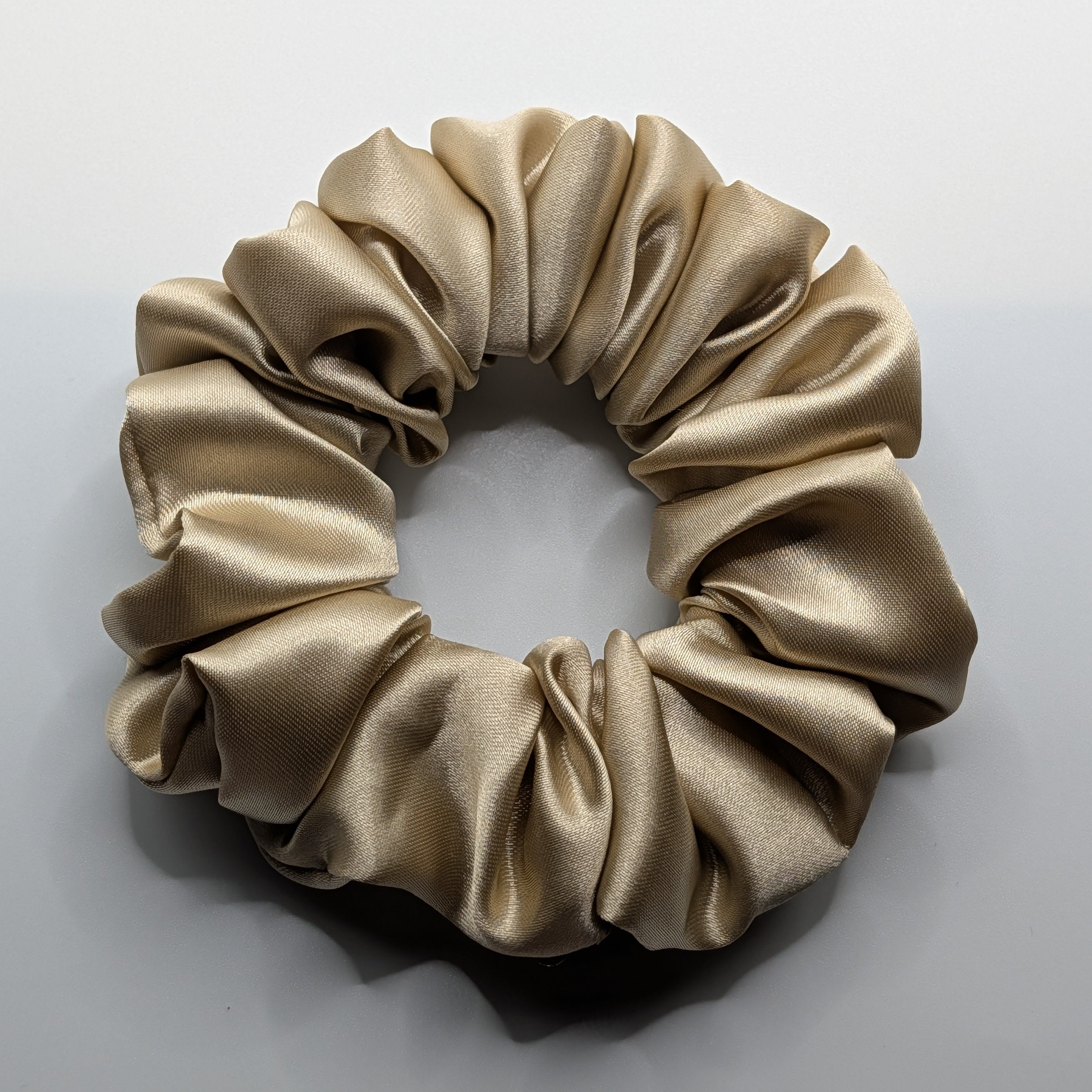 mittel - Soft champagne satin hair tie with elegant ruffles and shimmering fabric.

Weiches champagner-goldenes Haargummi mit eleganten Raffungen.