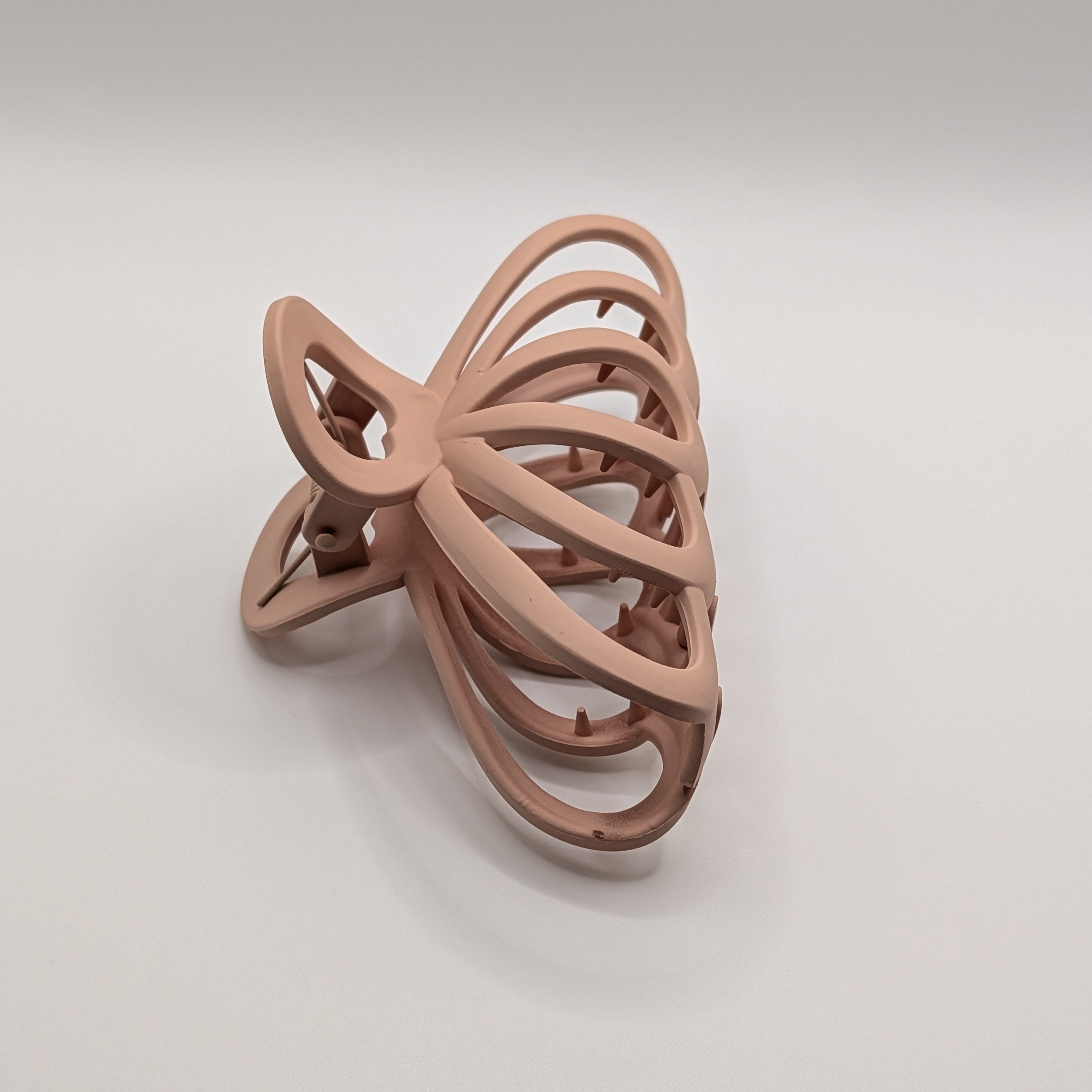 Roségold - Side angle view of the matte rose hair claw showing the curved teeth.	

Seitenansicht der matten rosa Haarklammer mit Fokus auf die geschwungenen Zinken.