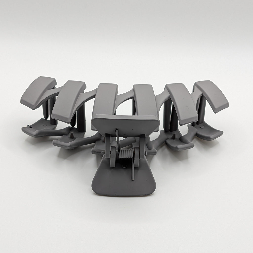 Grau - Close-up of the internal spring and wide-set teeth of a matte grey hair claw.

Detailansicht der Feder und der breiten Zinken einer matten grauen Haarklammer.