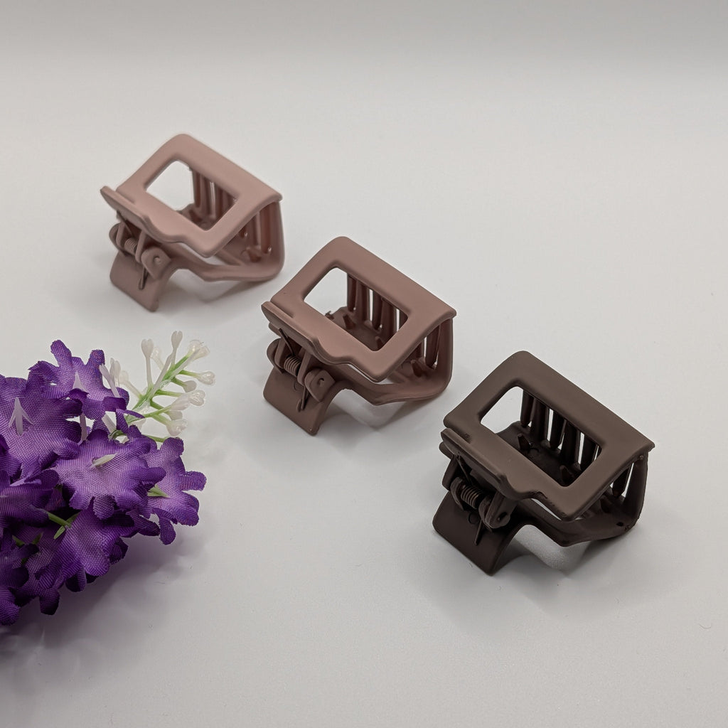 Three square geometric hair clips in dusty rose and brown shades next to purple flowers.

Drei eckige geometrische Haarklammern in Altrosa und Brauntönen neben lila Blumen.