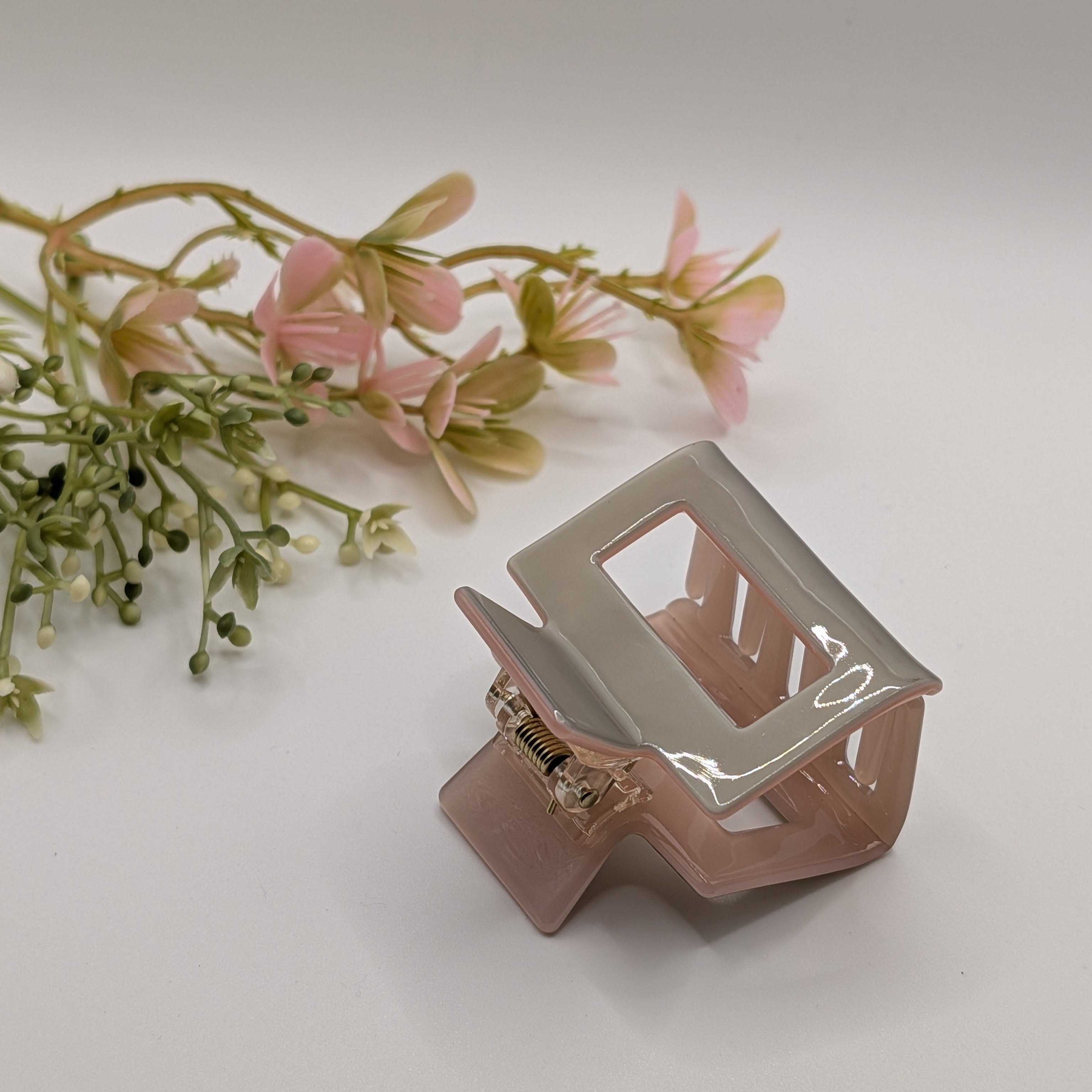 Rosé-Grau Duo - Haarspange „Classic-Pastell“ | Rosa-Grau Block - Mercy Haaraccessoires

Beige-pink hair clip decoratively arranged with a branch of pink artificial flowers in a bright atmosphere.

Close-up of an opened two-tone hair clip focusing on the sturdy gold metal mechanism.