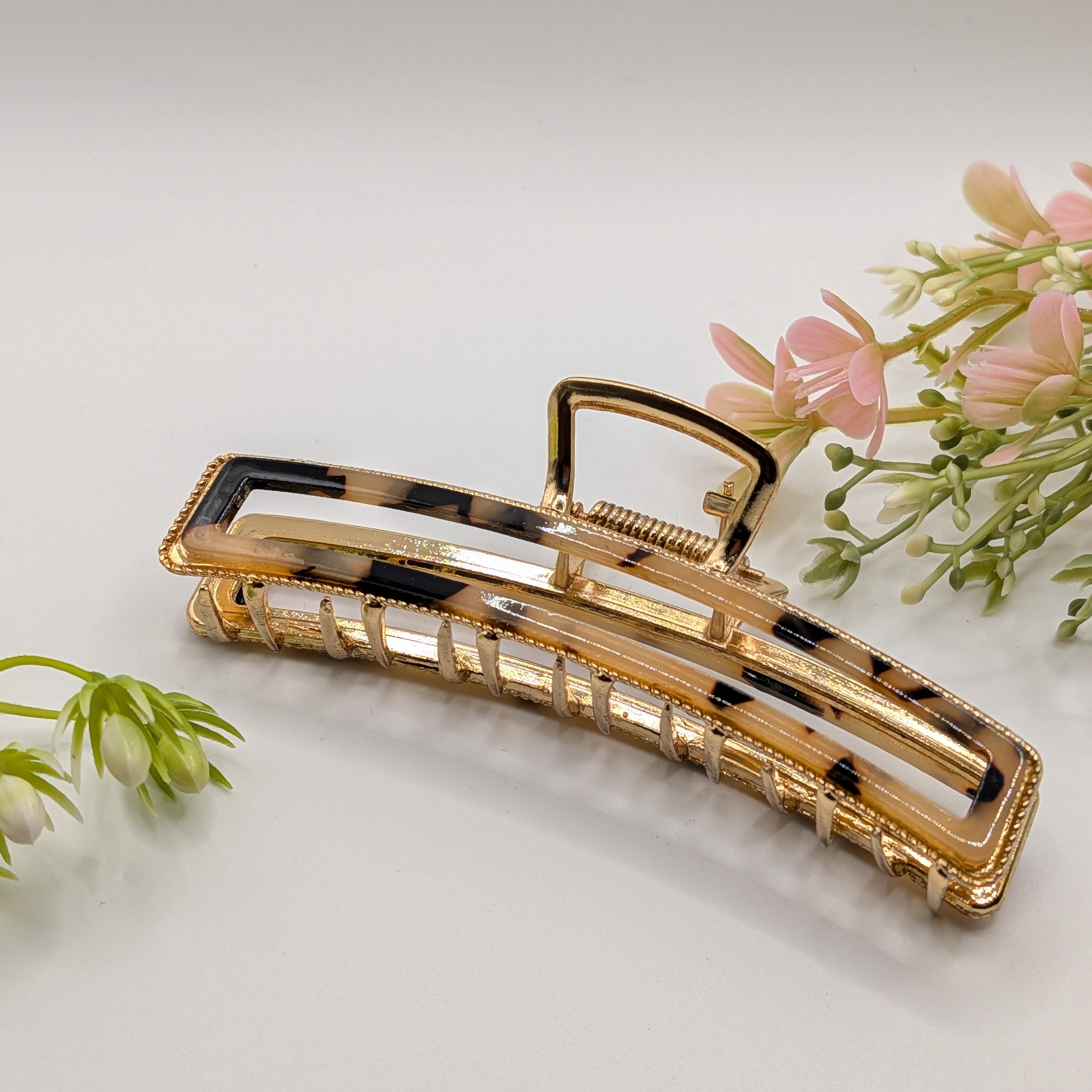 Klassisches Schildpatt - "Metallic Luxury" 11cm Haarspange - Mercy Haaraccessoires

Moderne goldene Haarklammer mit einem Inlay in braun-schwarzer Schildpatt-Optik, präsentiert neben zarten rosa Dekoblumen.