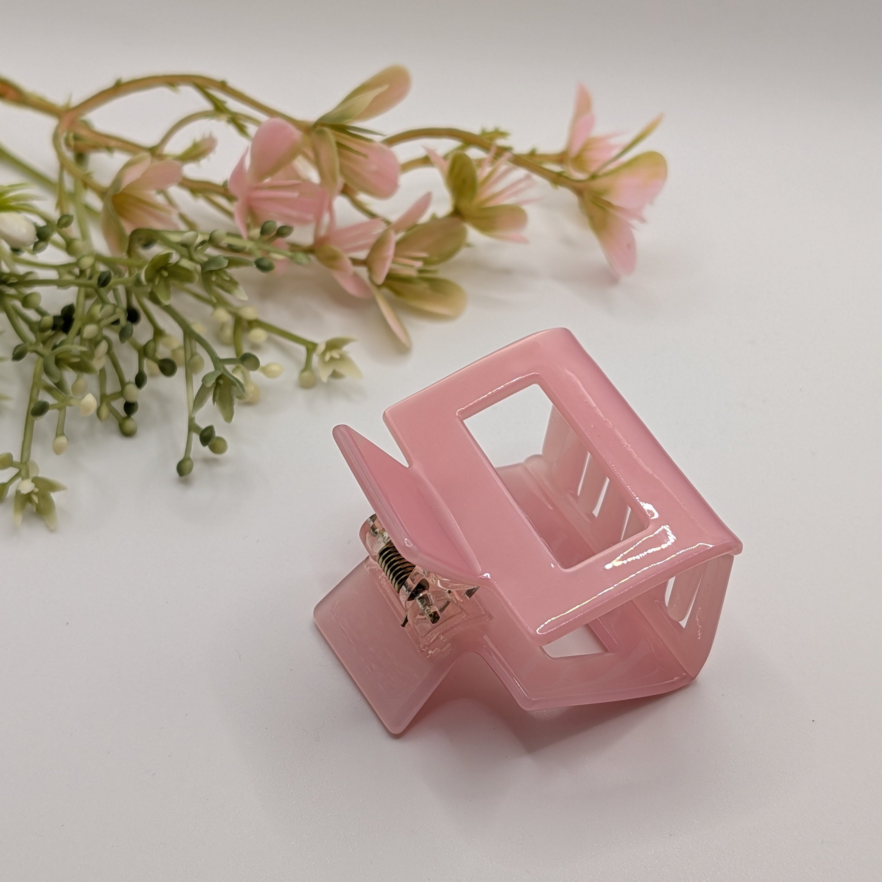 Pastellrosa - Haarspange „Classic Rosé“ | Transluzentes Hellrosa - Mercy Haaraccessoires

Eine pastellrosa, rechteckige Haarklammer aus glänzendem Kunststoff, dekorativ platziert neben zarten Kunstblumen auf hellem Untergrund.