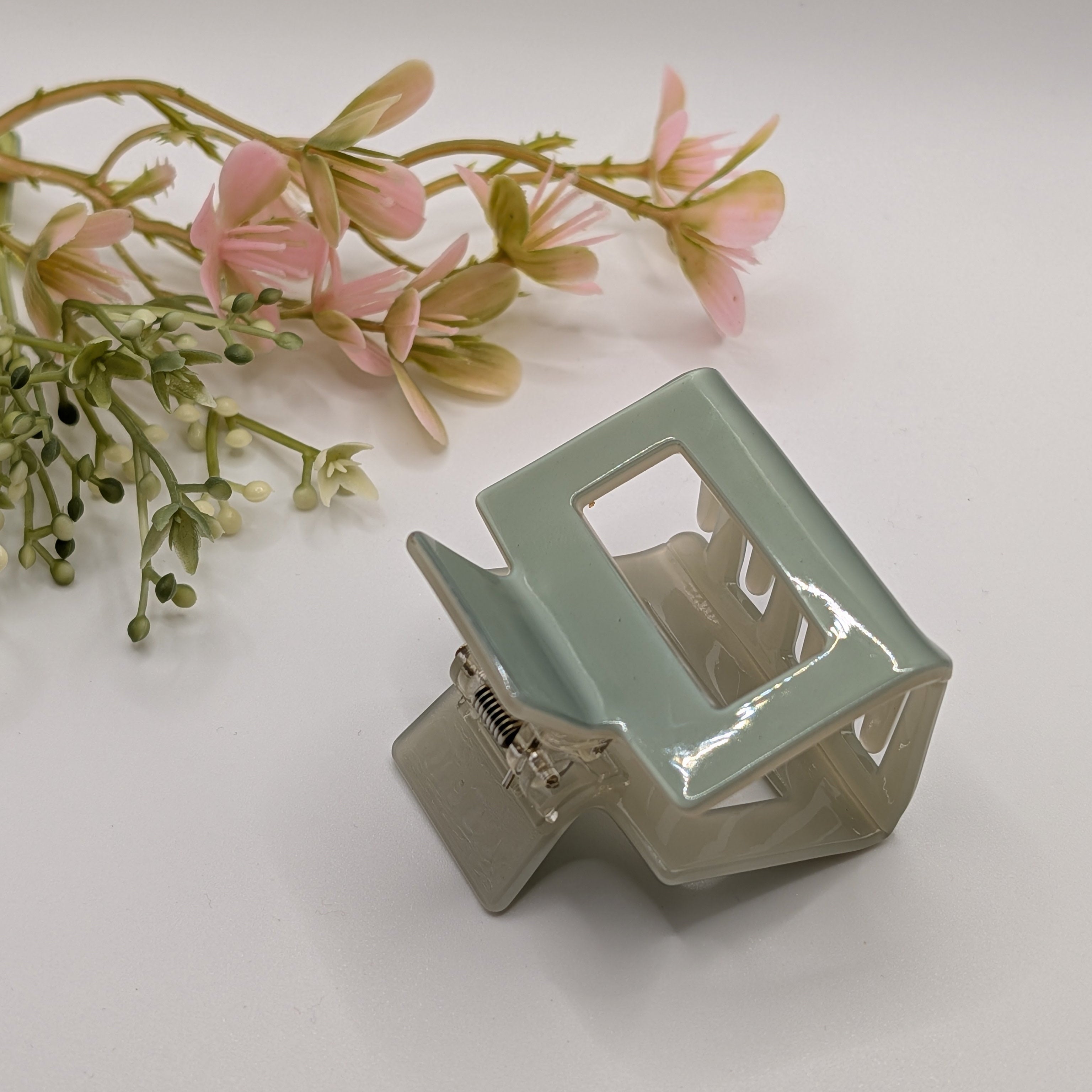 Salbeigrün Duo - Haarspange „Classic-Mint“ | Minz-Beige Block - Mercy Haaraccessoires

Salbeigrüne Haarklammer ästhetisch präsentiert neben einem dekorativen Zweig mit rosa Blüten.