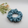 3er Set - Top view of a medium blue satin scrunchie on a white background.	

Draufsicht eines mittelgroßen blauen Satin-Haargummis auf weißem Hintergrund.