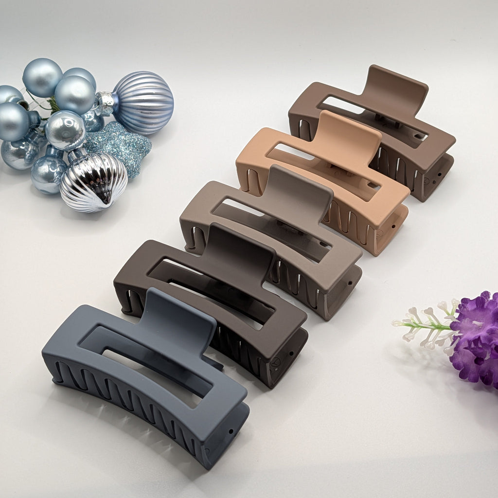 A set of five large 8cm rectangular matte hair claw clips in neutral shades arranged diagonally on a white surface with blue ornaments.	

Ein Set aus fünf großen 8 cm langen, rechteckigen, matten Haarklammern in neutralen Tönen, diagonal angeordnet.