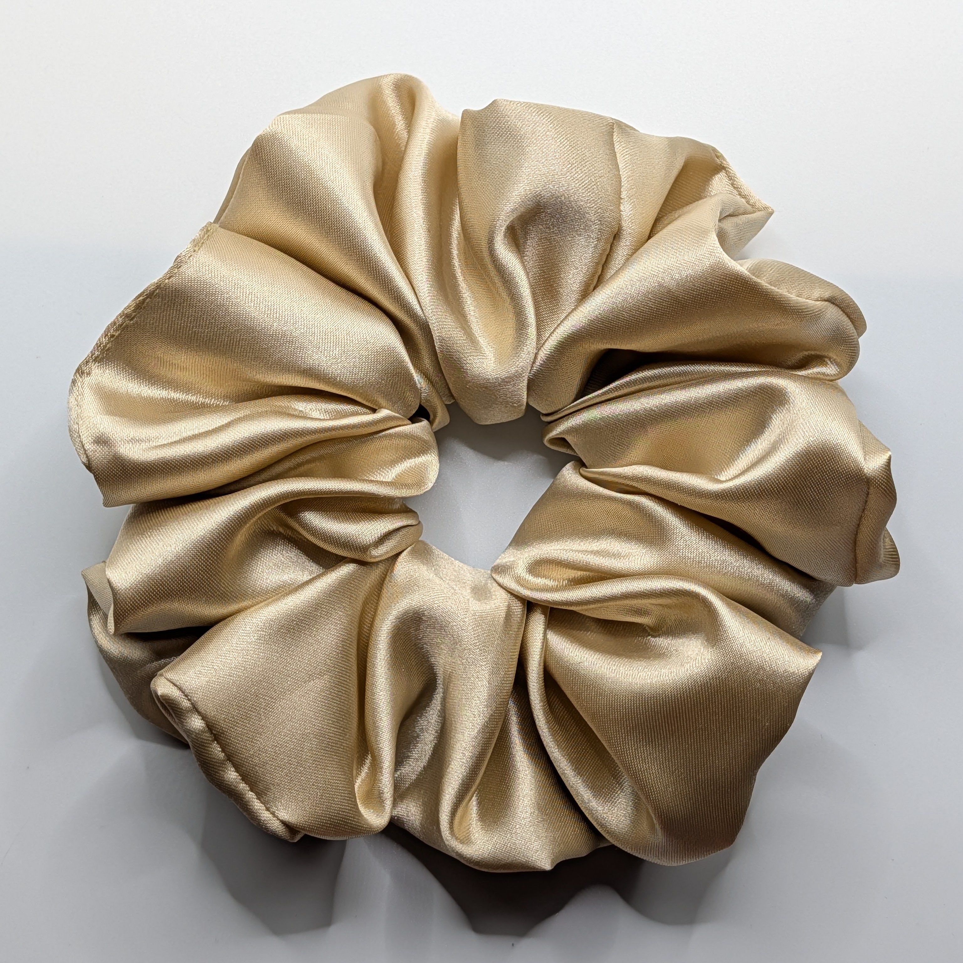 groß - Close-up of a large oversized champagne satin scrunchie with high shine.	

Nahaufnahme eines großen XL Satin-Haargummis in Champagner.