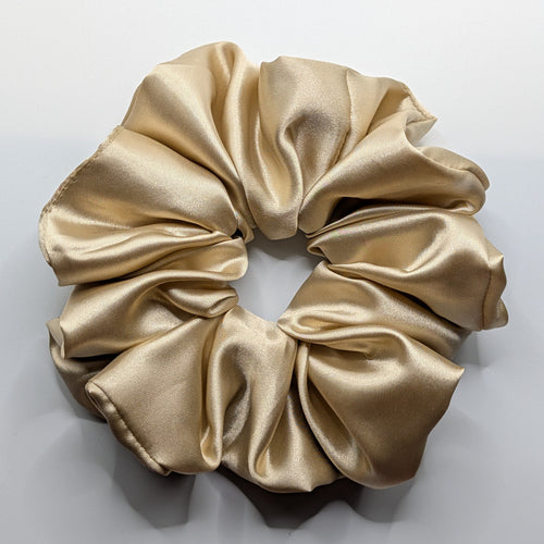 groß - Close-up of a large oversized champagne satin scrunchie with high shine.	

Nahaufnahme eines großen XL Satin-Haargummis in Champagner.