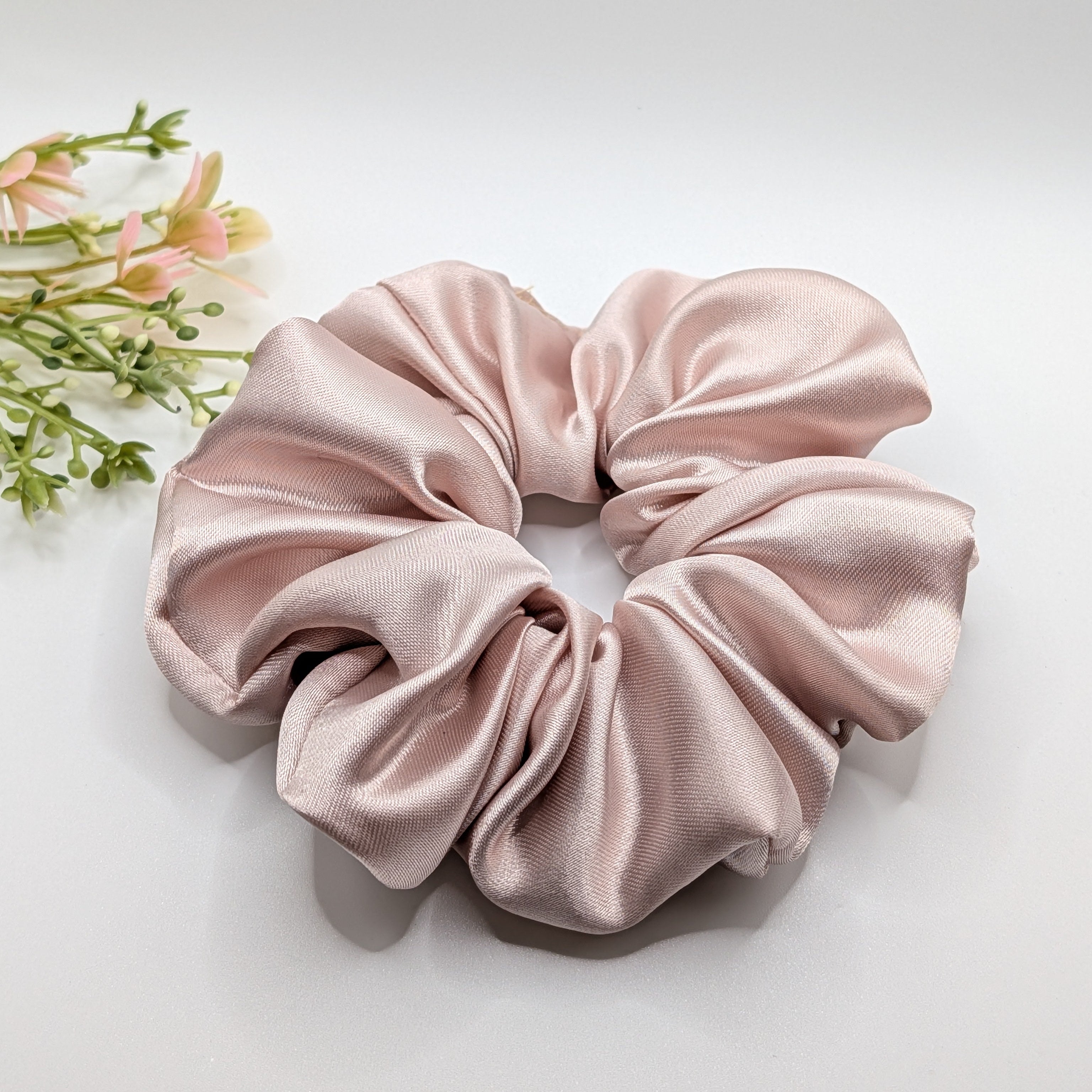 3er Set - Close up of a large luxury champagne rose satin scrunchie with decorative flowers.

Nahaufnahme eines großen Luxus-Satin-Haargummis in Champagner-Rosa mit Deko-Blumen.