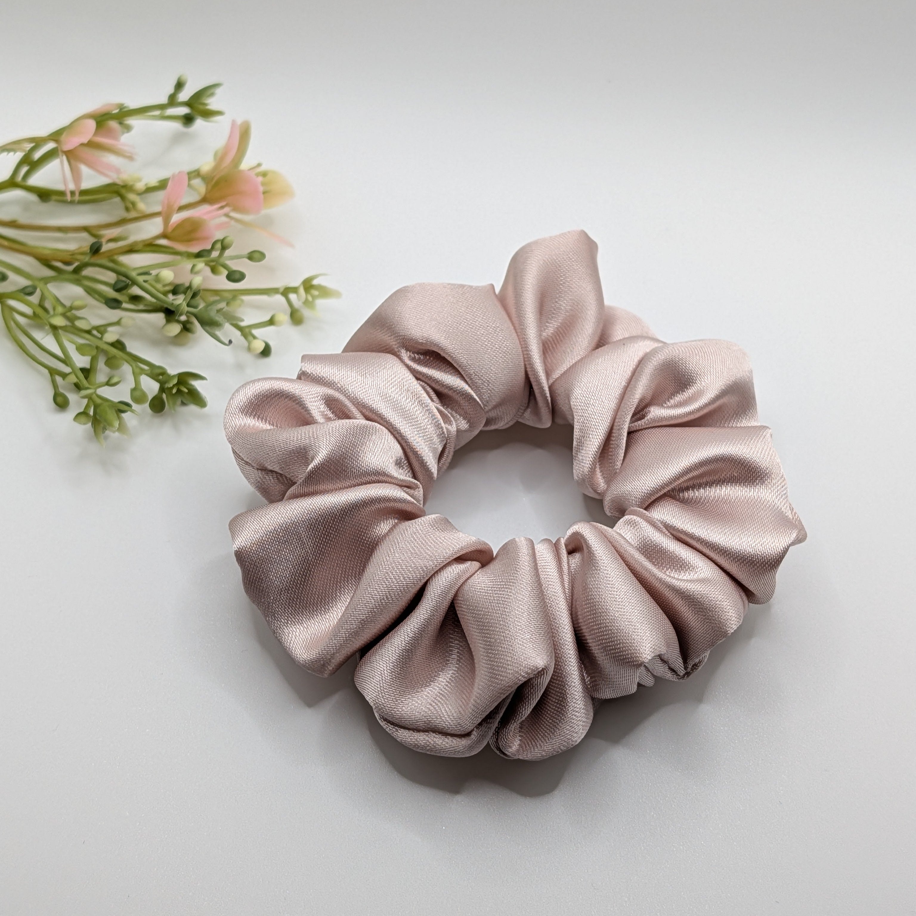 3er Set - Luxury champagne rose satin scrunchie placed with flowers.	

Luxuriöser Satin-Scrunchie in Champagner-Rosa mit Blumen dekoriert.