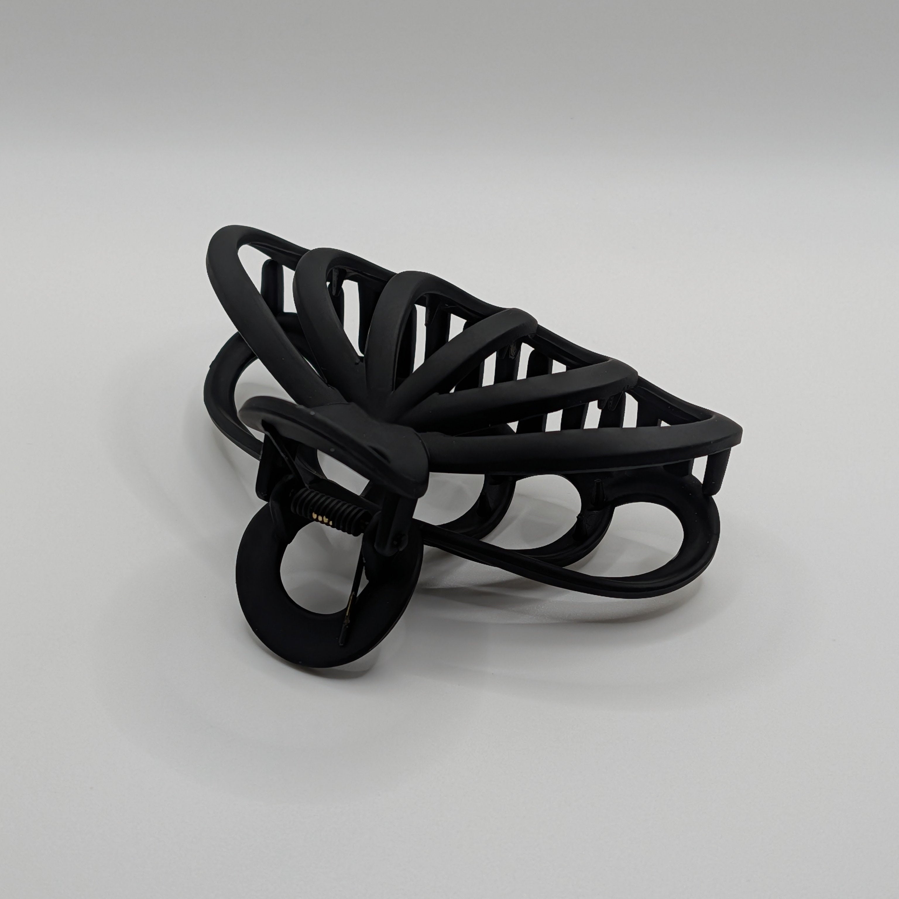 Schwarz - Close-up of the spring mechanism and handle of the matte black hair clip.

Nahaufnahme des Federmechanismus und des Griffs der mattschwarzen Haarspange.