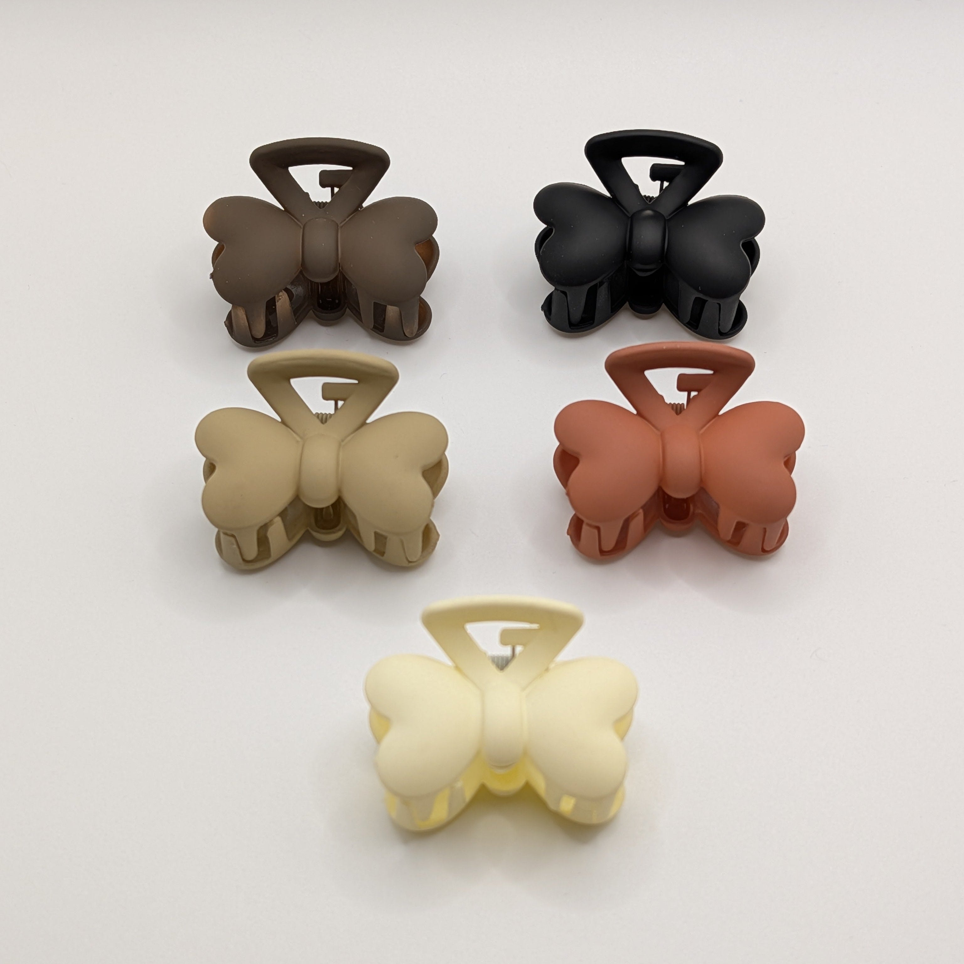 Flat lay of five butterfly-shaped matte hair claw clips in black, brown, tan, terracotta, and cream.

5er-Set matte Schmetterlings-Haarklammern in Schwarz, Braun, Beige, Terrakotta und Creme.
