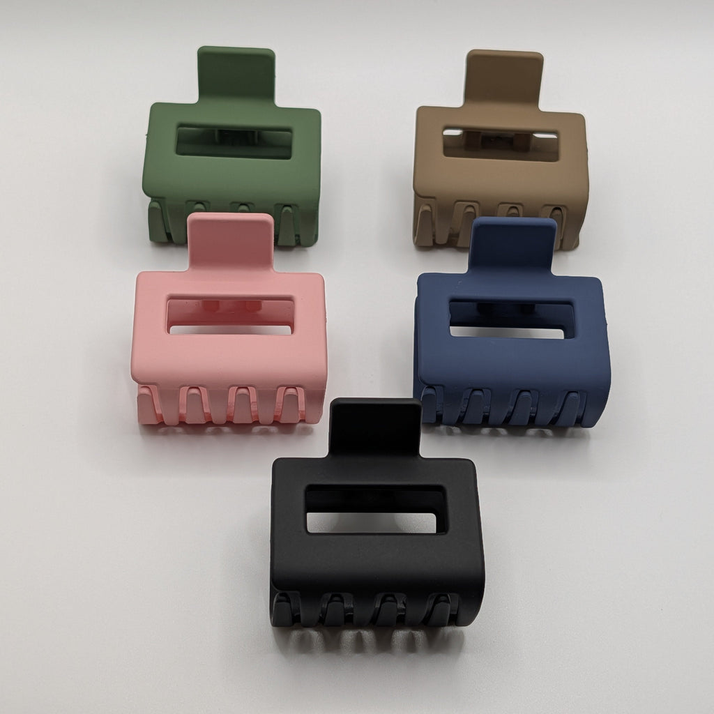 Professional flat lay of five 5cm rectangular matte hair claw clips in green, tan, pink, blue, and black.	

Draufsicht auf fünf 5 cm lange eckige Haarklammern in Grün, Beige, Rosa, Blau und Schwarz.