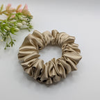3er Set - Medium sized champagne gold satin scrunchie next to decorative flowers.

Mittelgroßes champagnerfarbenes Satin-Haargummi neben Blumen.