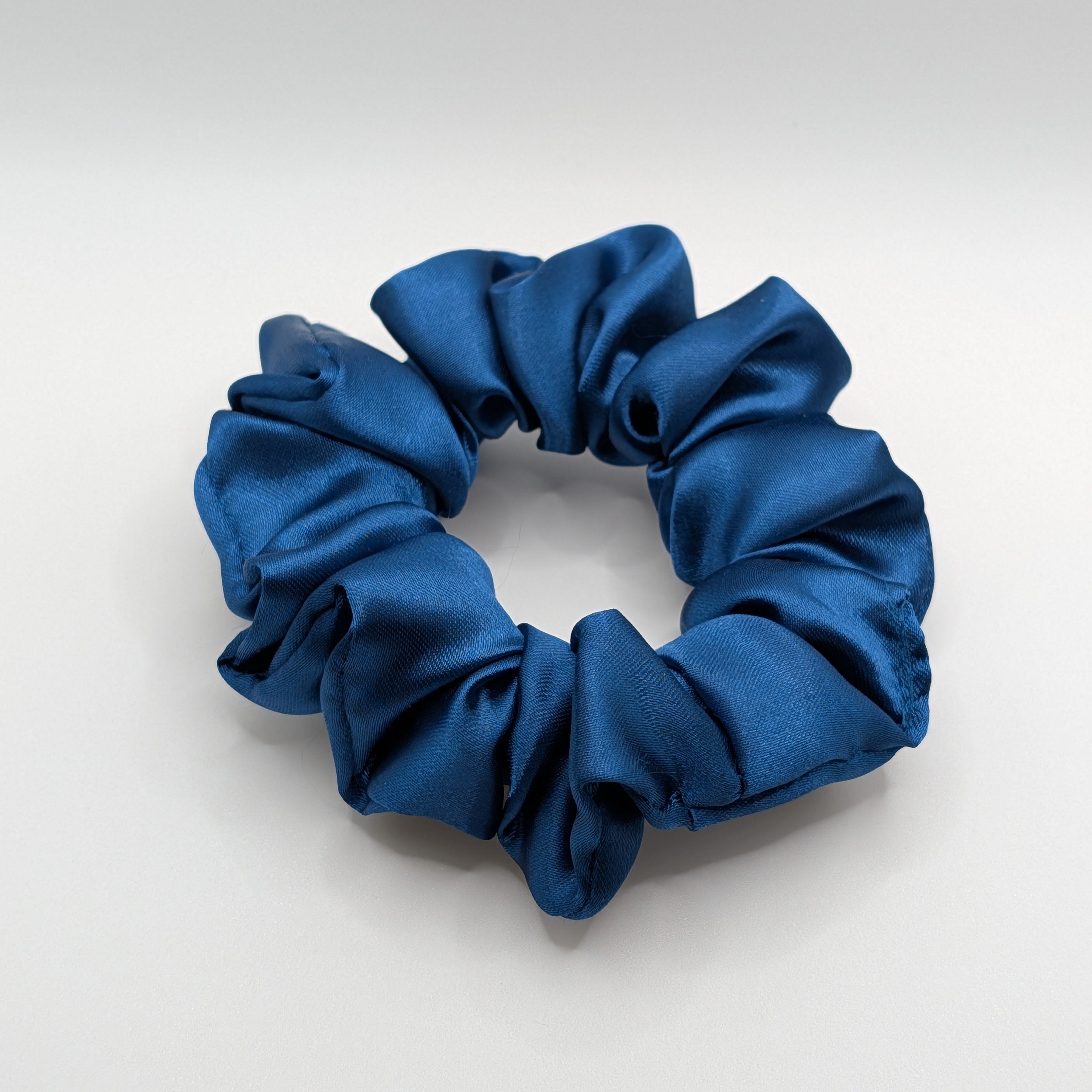 mittel - Side angle of a medium navy satin scrunchie showing volume and shine.	

Seitenansicht eines mittleren blauen Satin-Scrunchies zeigt Volumen und Glanz.