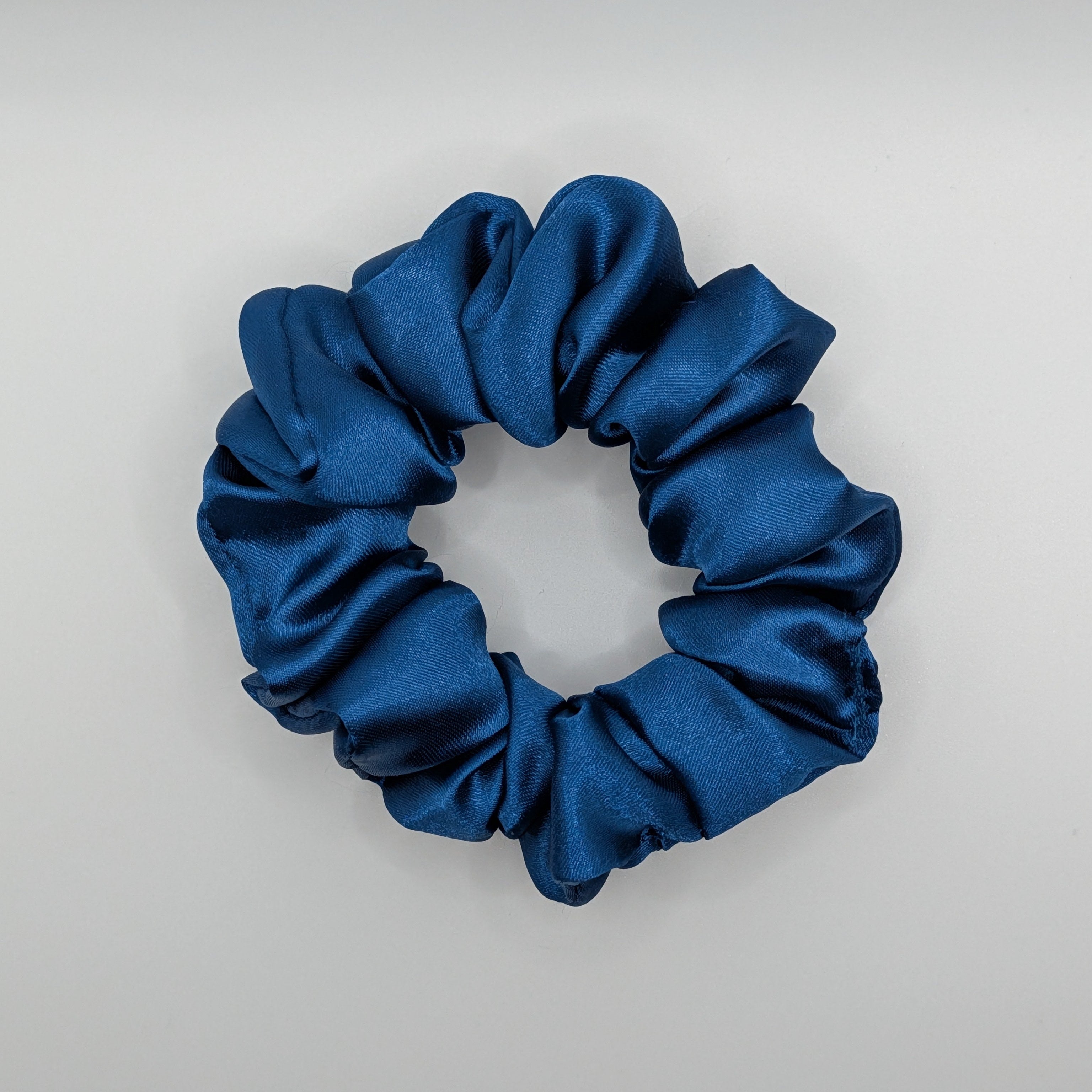mittel - Side angle of a medium navy satin scrunchie showing volume and shine.	

Seitenansicht eines mittleren blauen Satin-Scrunchies zeigt Volumen und Glanz.