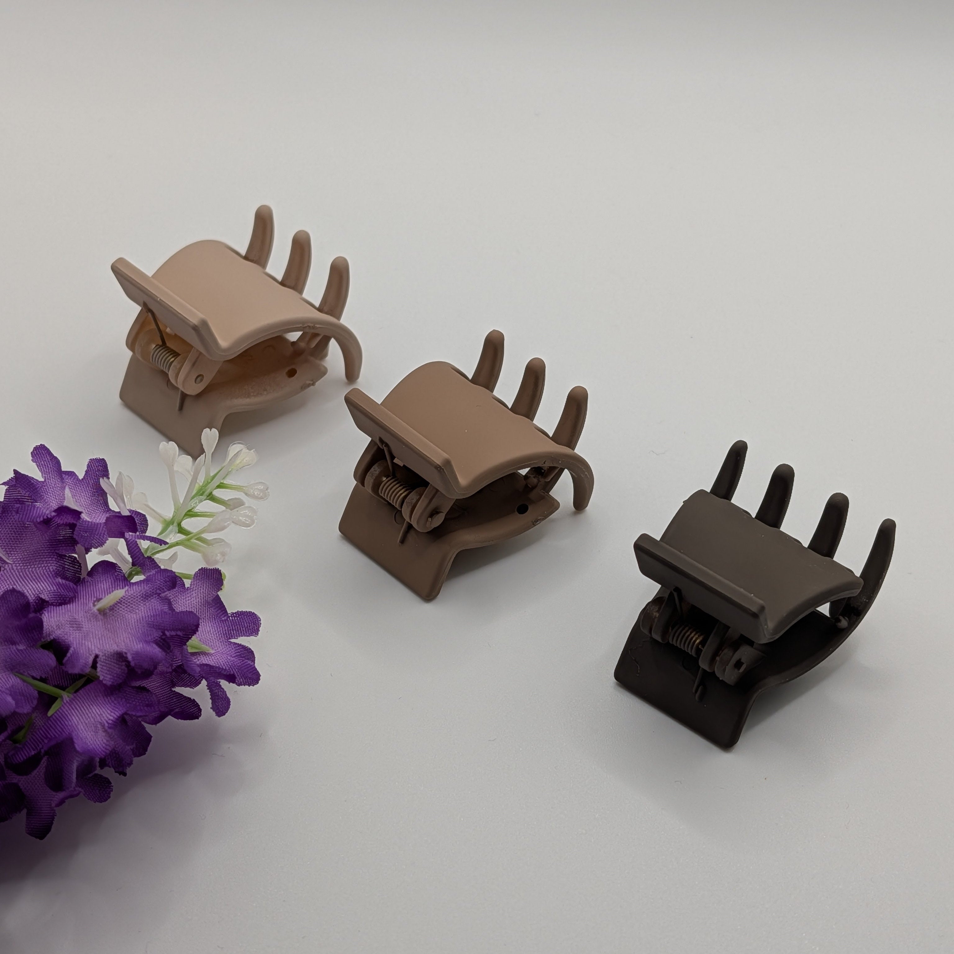 Three small 3cm matte hair claw clips in beige and brown shades next to purple flowers.

Drei kleine 3cm matte Haarklammern in Beige- und Brauntönen neben lila Blumen.