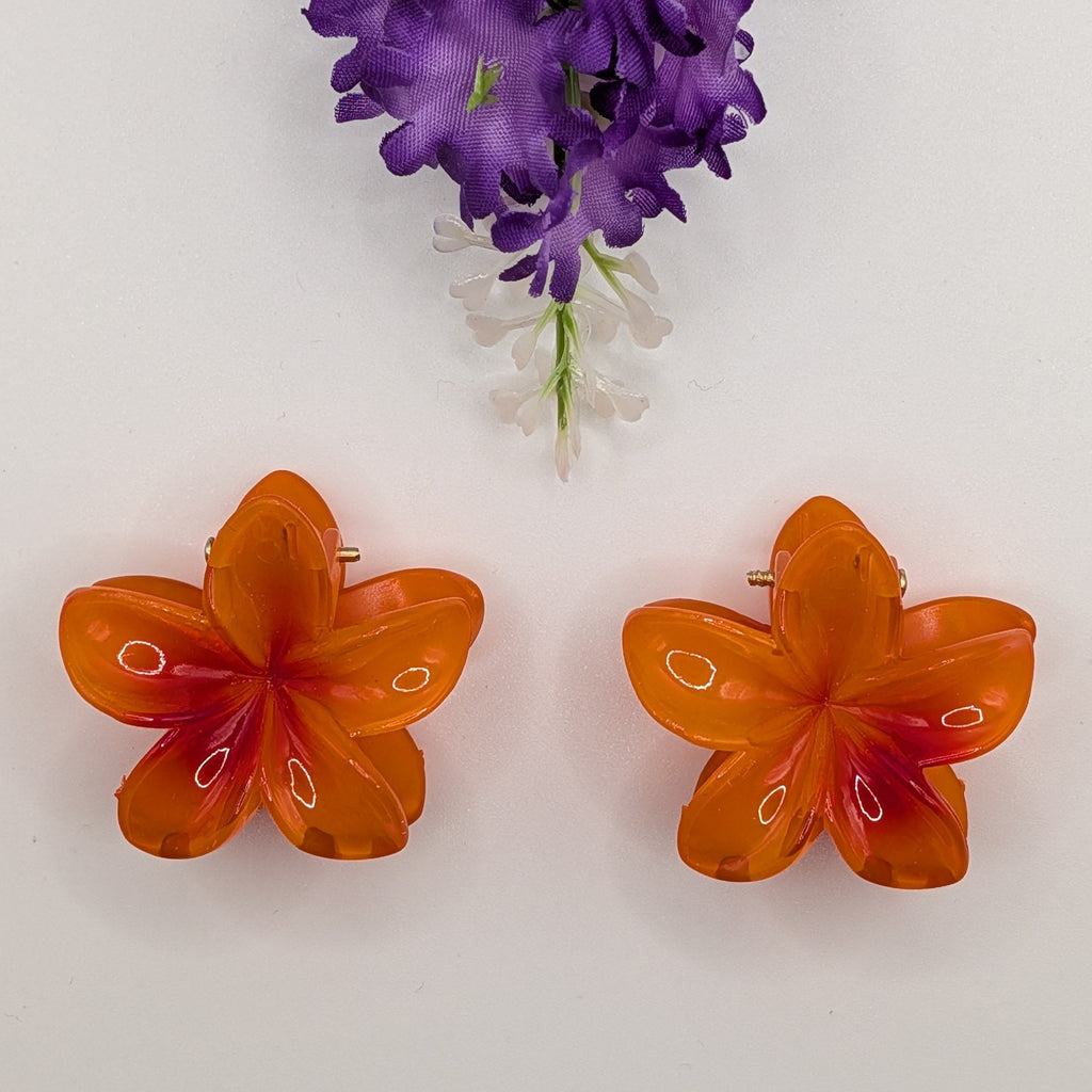 Leuchtendes Orange - Flat lay of two small vibrant orange flower hair claws with purple floral accents.	

Flat-Lay von zwei kleinen leuchtend orangefarbenen Blumen-Haarklammern mit lila Blumenakzenten.