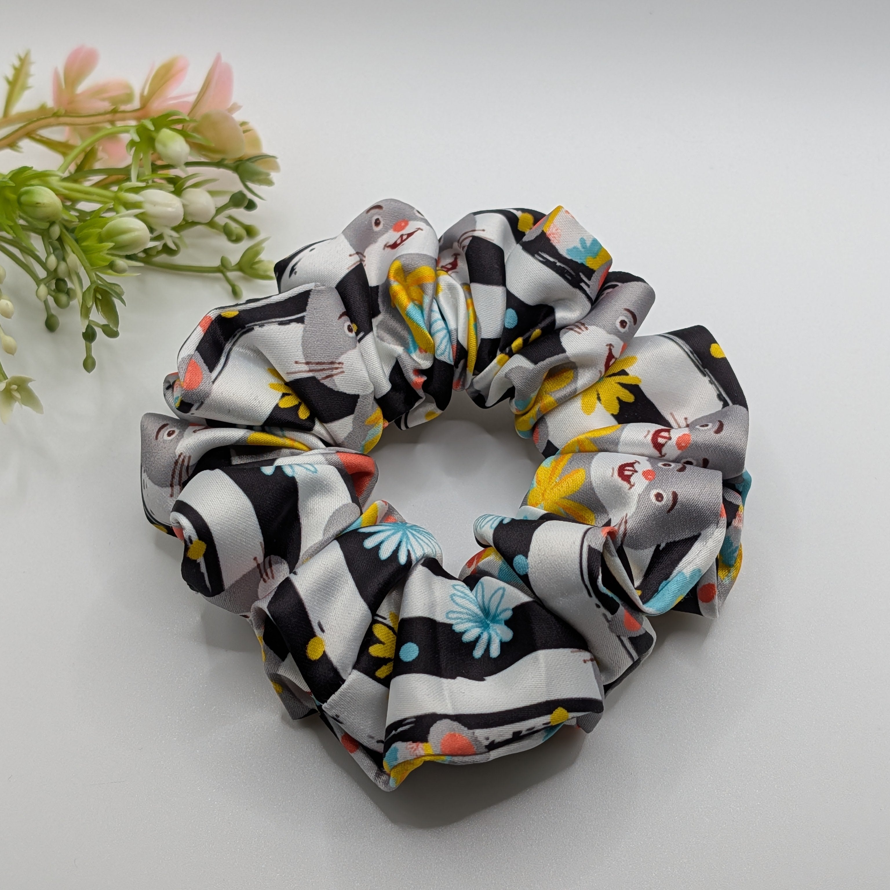 mittel - Rabbit print satin scrunchie laid flat next to decorative flowers.	

Satin-Haargummi mit Hasen-Print neben dekorativen Blumen.