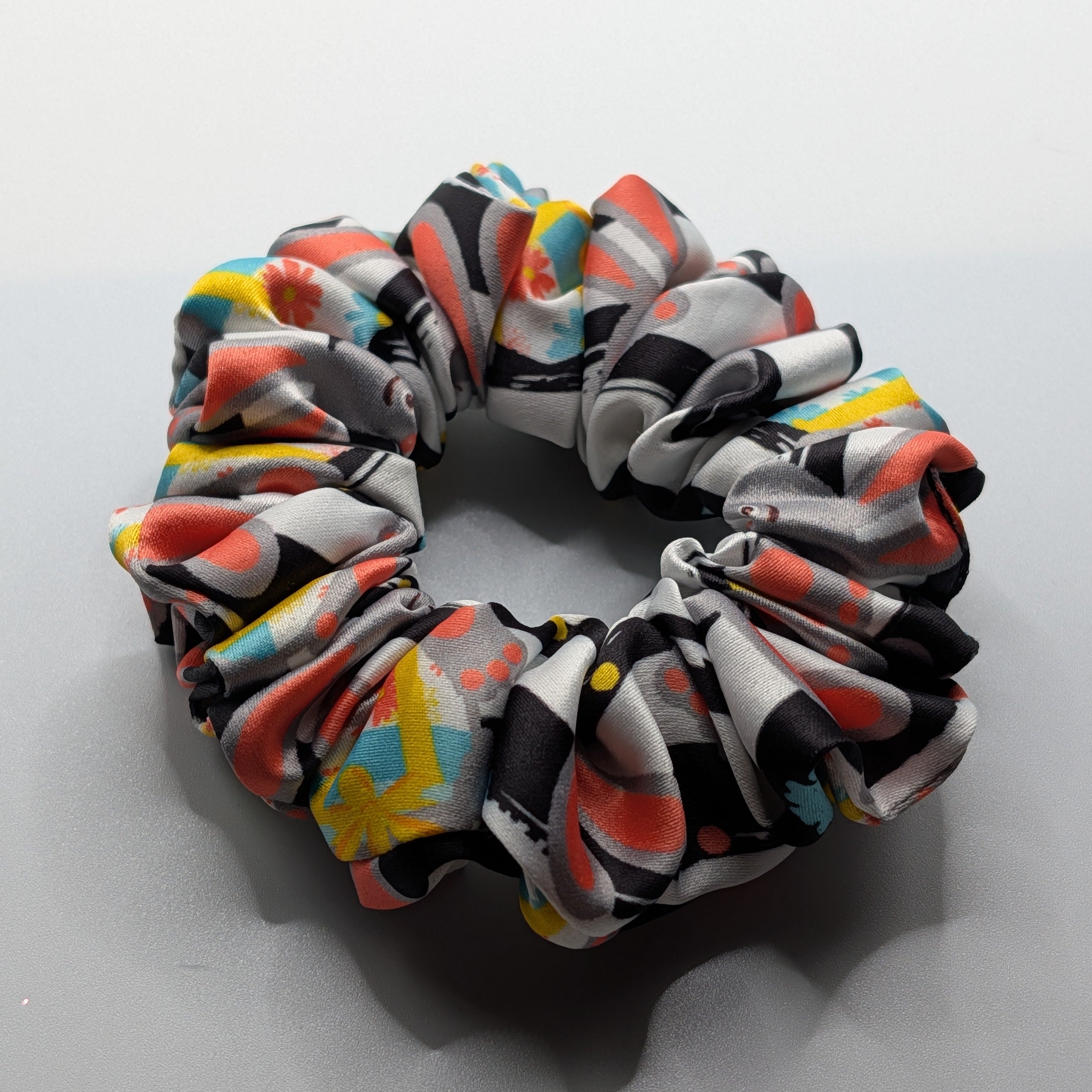 klein - Rabbit print satin scrunchie laid flat next to decorative flowers.	

Satin-Haargummi mit Hasen-Print neben dekorativen Blumen.