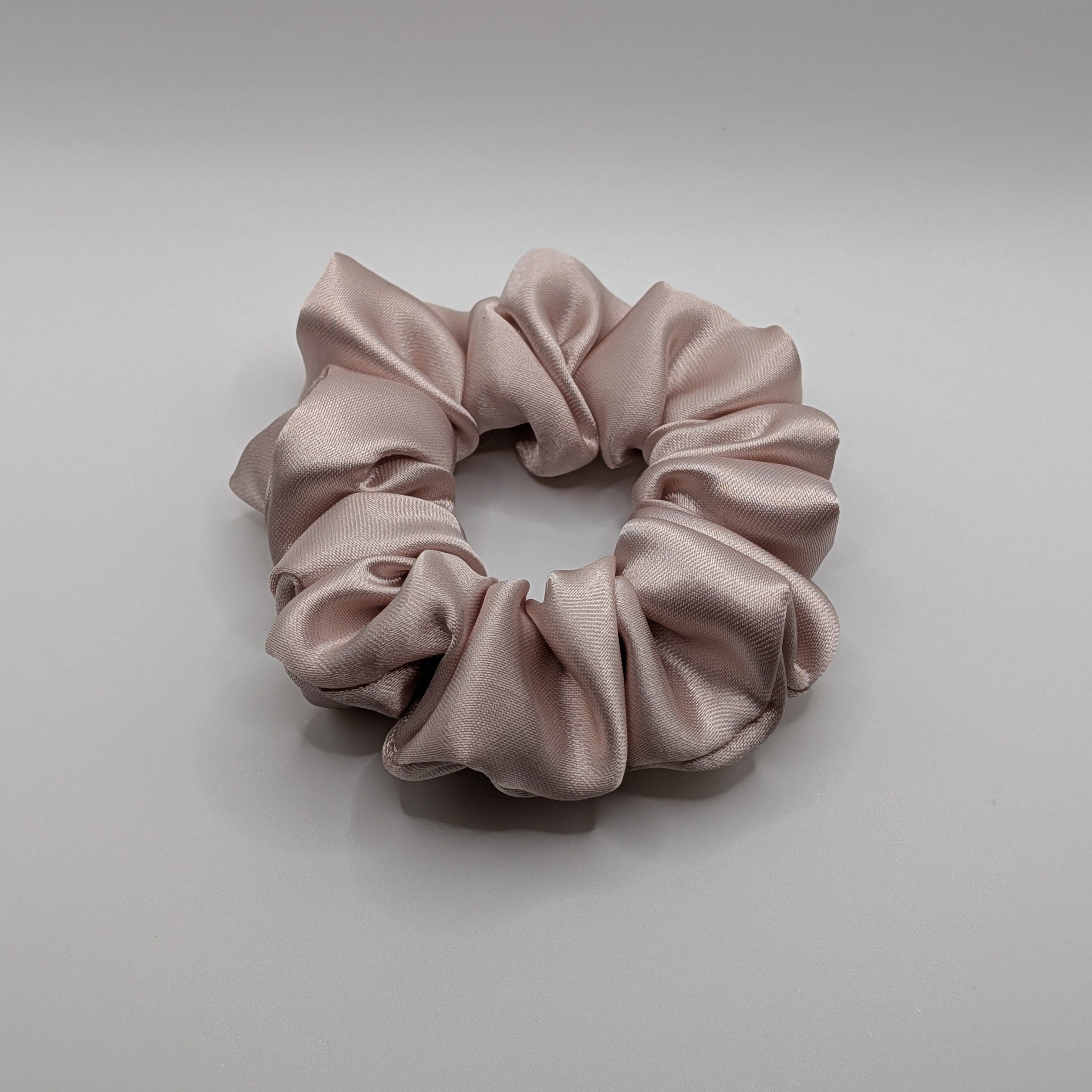 mittel - Medium champagne rose satin scrunchie on white background.	

Mittleres Satin-Haargummi in Champagner-Rosa auf weißem Hintergrund.