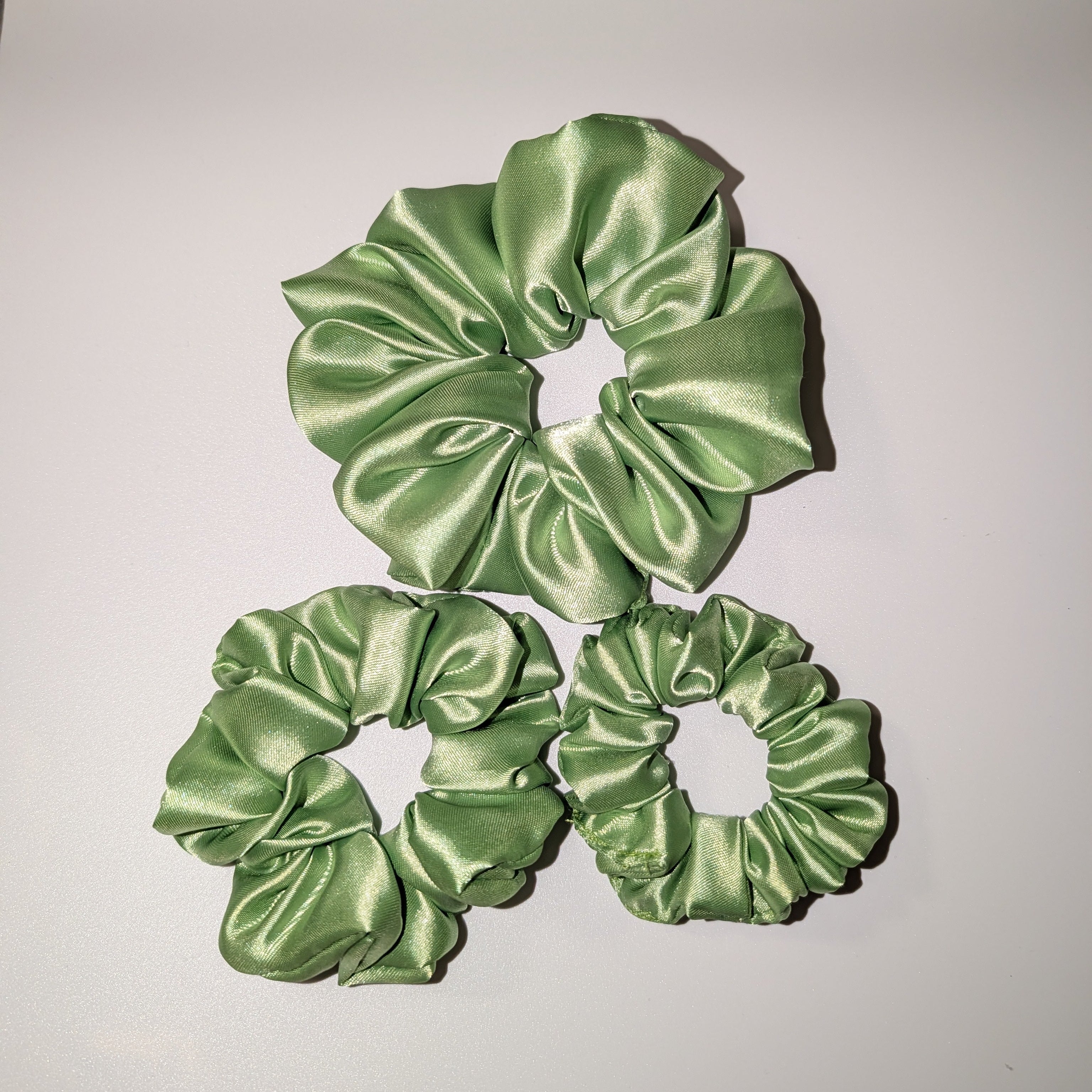 Set of 3 sage green satin scrunchies in small, medium, and large sizes.

3er-Set Satin-Haargummis in Salbeigrün in den Größen Klein, Mittel und Groß.