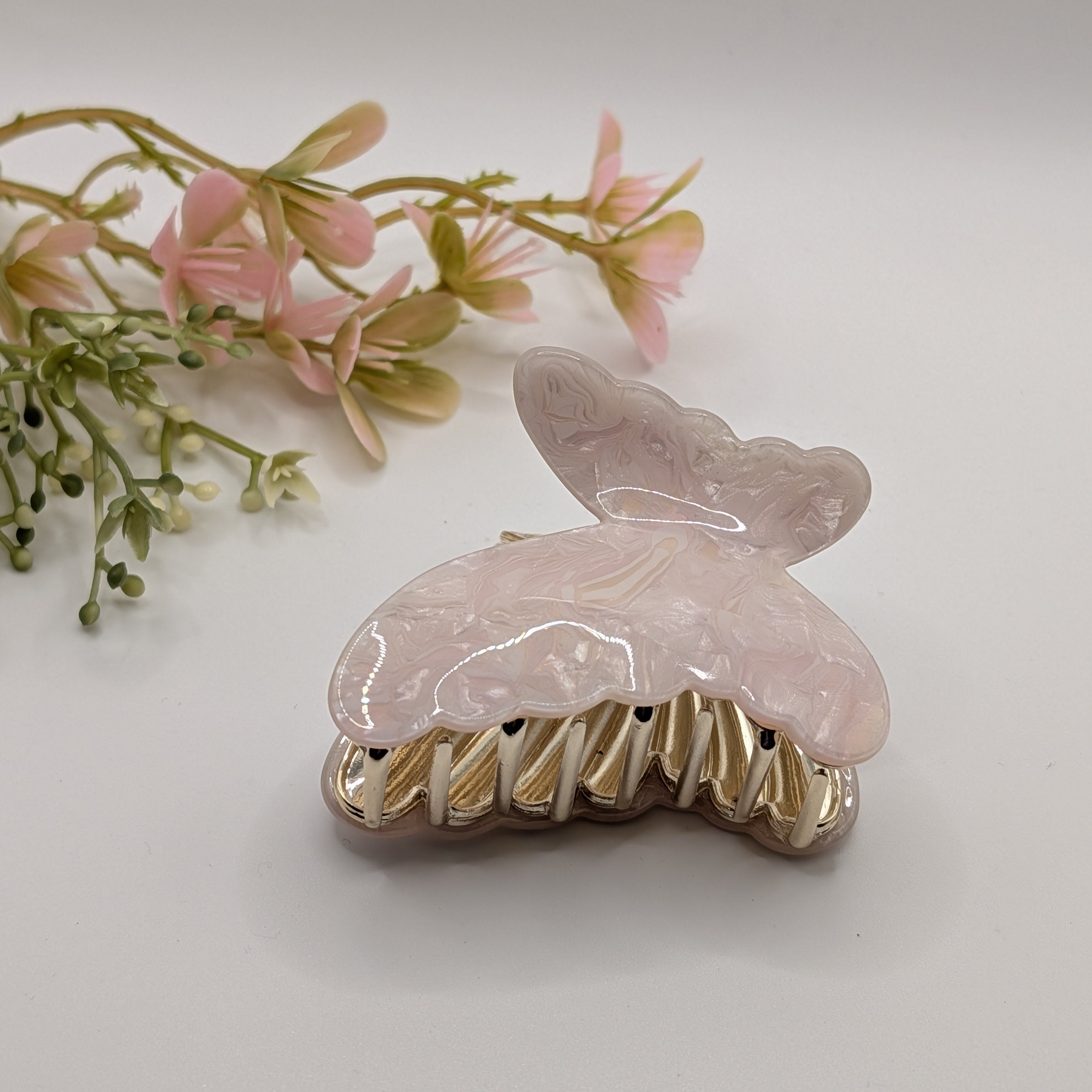 Perlglanz Rosa - Haarspange „Pink Angel“ | Rosé-Quarz-Marmor - Mercy Haaraccessoires

Eine rosa marmorierte Schmetterlings-Haarklammer in der Seitenansicht mit goldenen Zinken, dekoriert neben rosa Blumen.