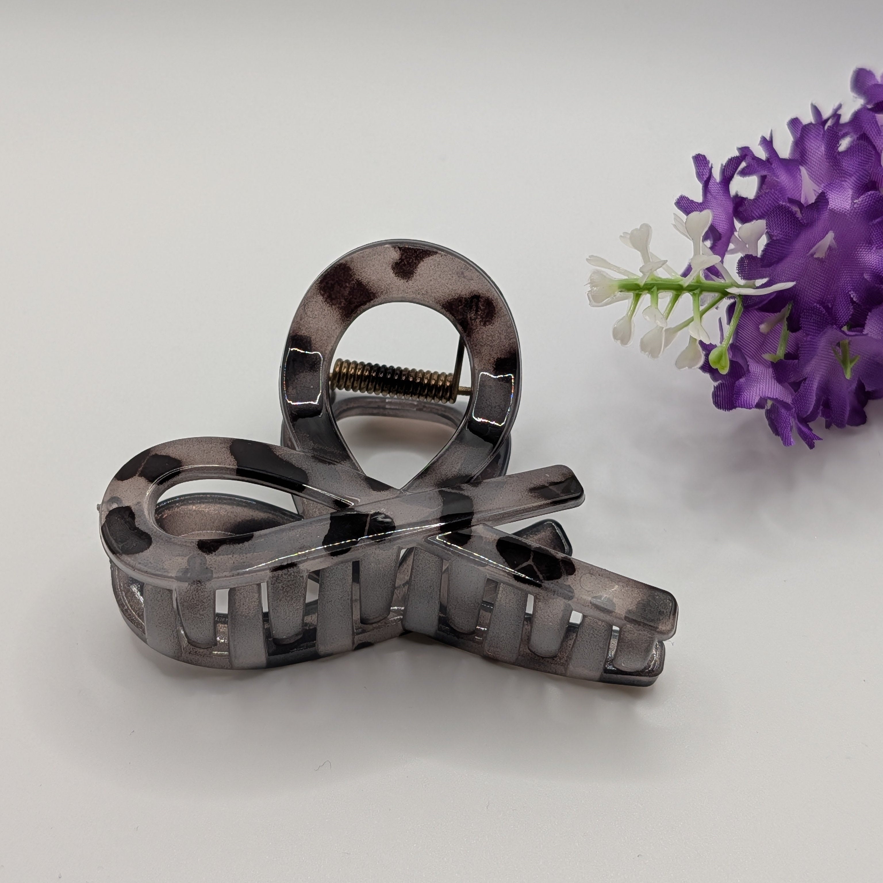 Grau - Silver leopard print hair claw displayed next to purple flowers.

Silberne Haarklammer mit Leopardenmuster, präsentiert neben lila Blumen.