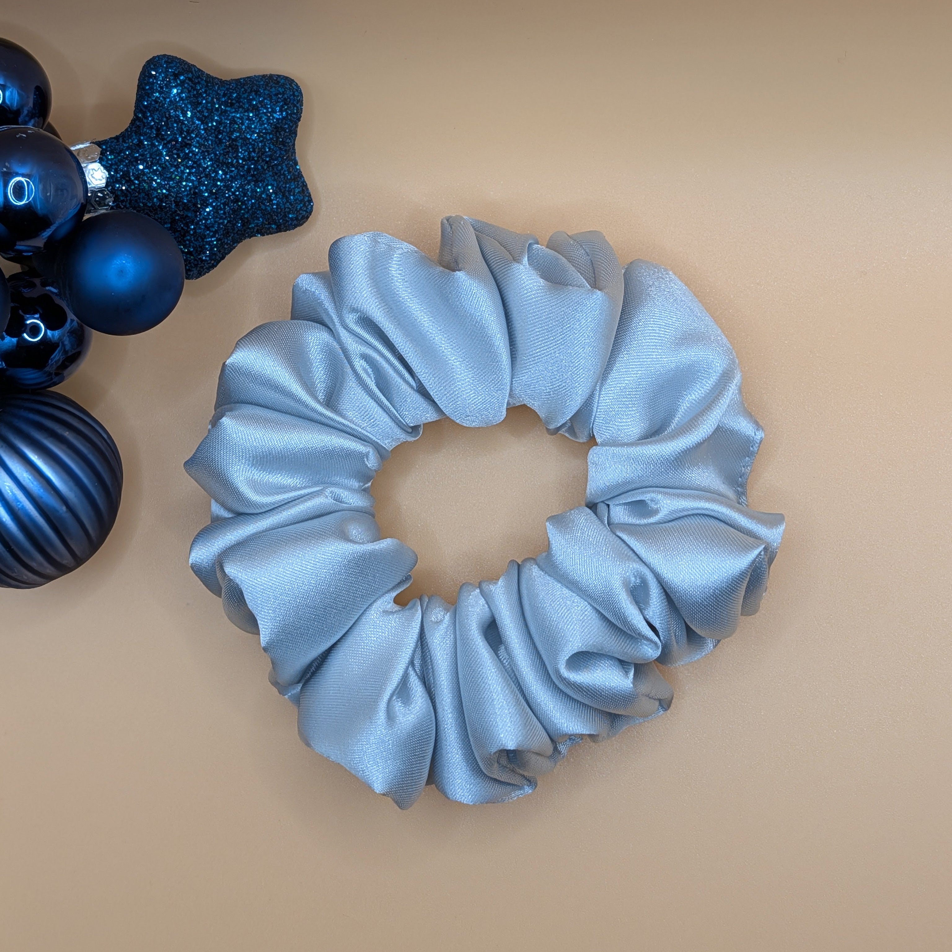 mittel - Top-down view of a medium silver satin hair tie.

Draufsicht auf ein mittlgroßes silbernes Satin-Haargummi.