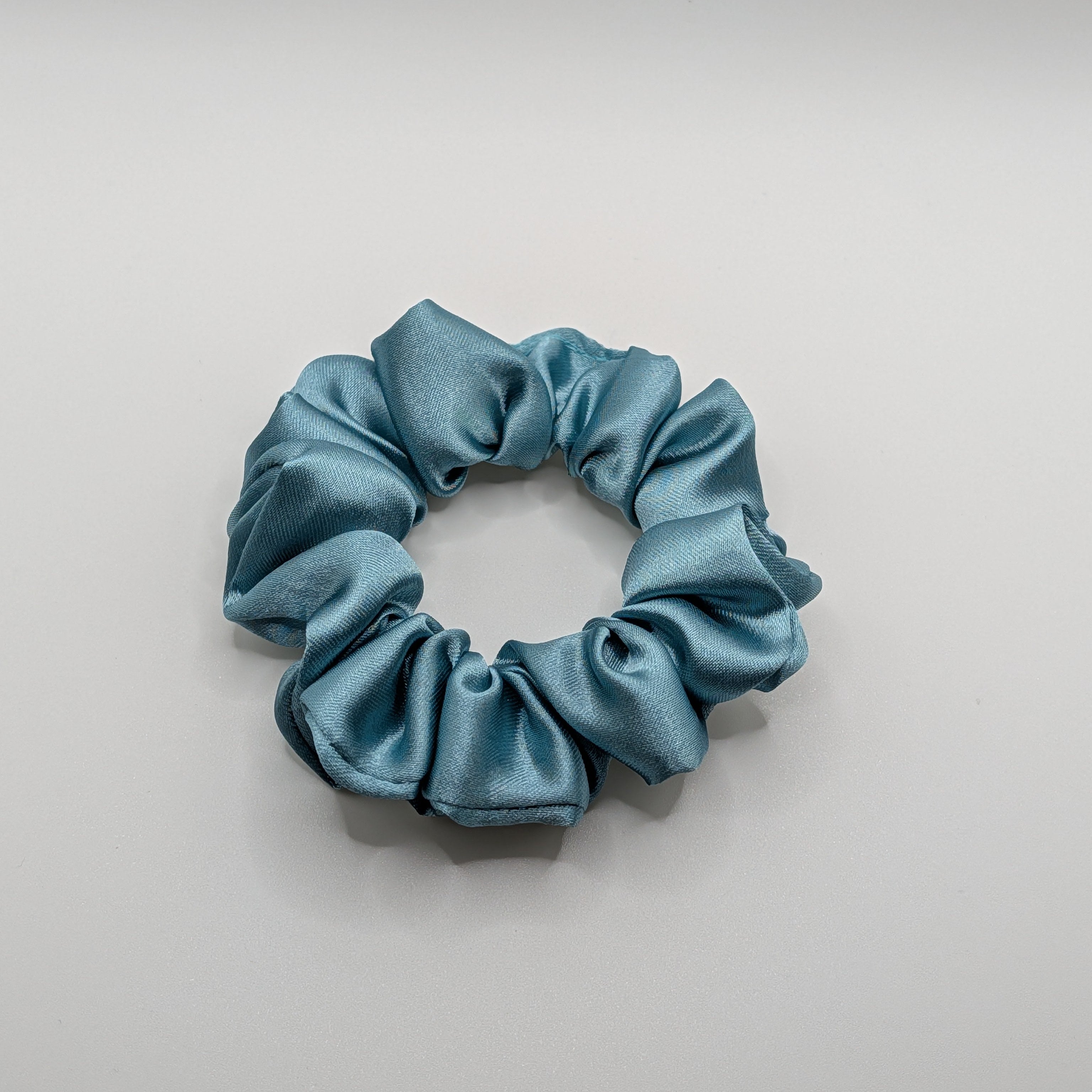 klein - Minimalist view of a small blue satin hair scrunchie.

Minimalistische Ansicht eines kleinen blauen Satin-Haargummis.