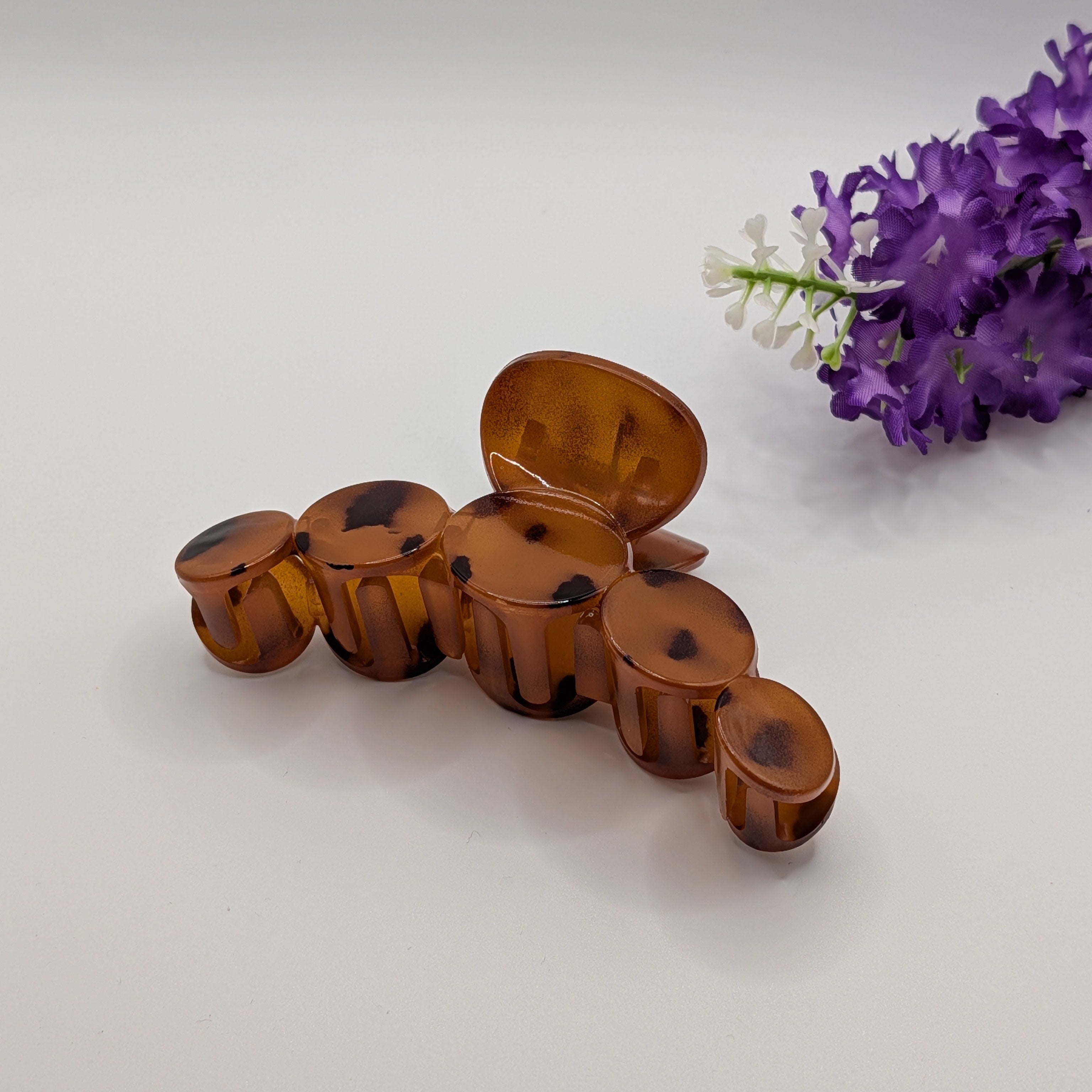 Dunkles Schildpatt - Side view of a large tortoiseshell patterned hair claw clip with purple floral background.

Seitenansicht einer großen Haarklammer mit Schildpatt-Muster und violettem Blumendekor im Hintergrund.